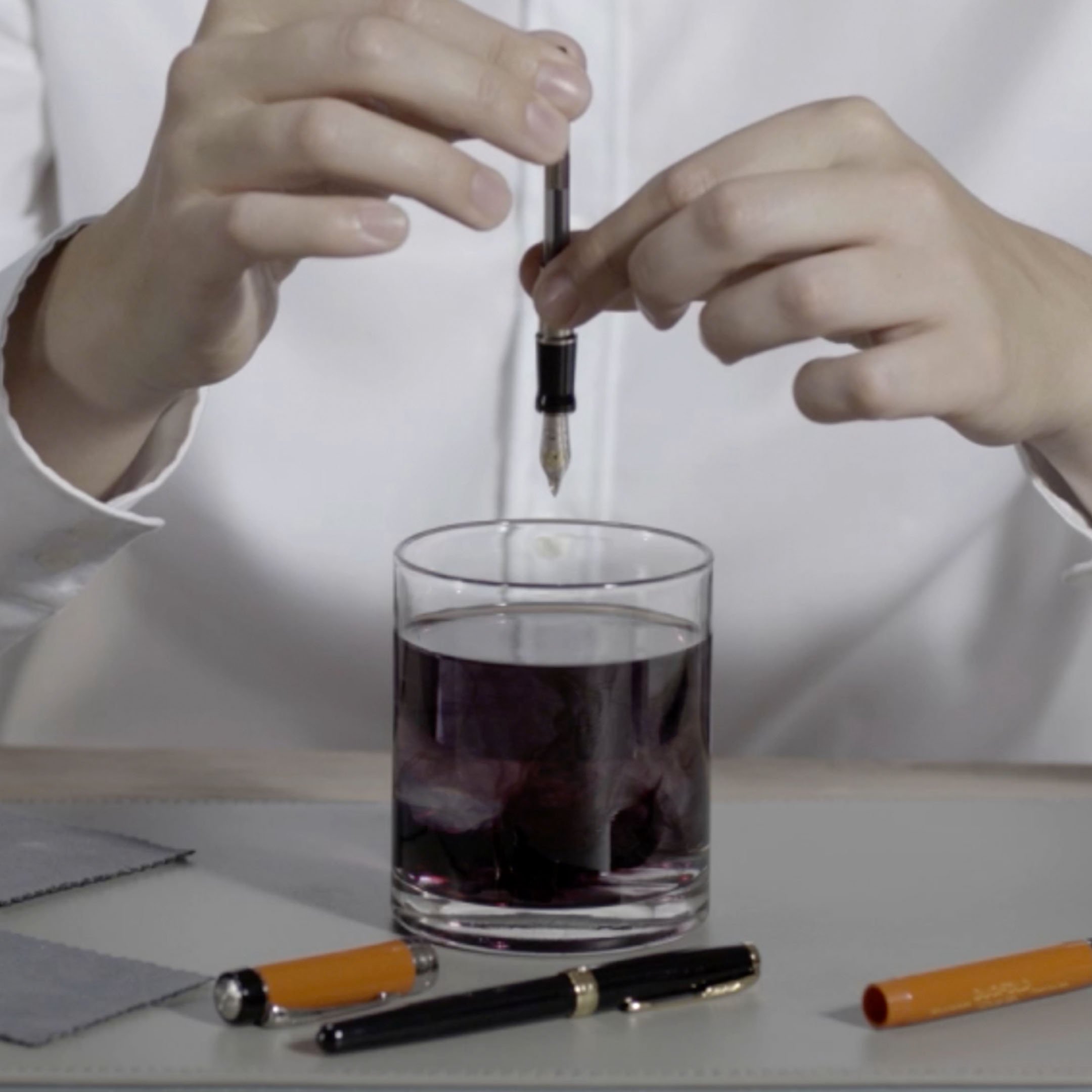 Two hands draining a fountain pen into a glass.